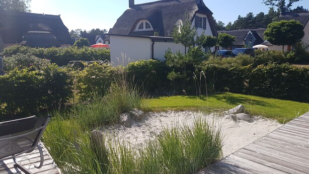 Un jardín con terraza de madera, un banco y un estanque rodeado de vegetación.