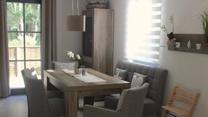 Un comedor con mesa de madera, sillas tapizadas en gris, lámpara colgante y un aparador de madera.