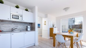 Une cuisine moderne avec des meubles blancs, un four à micro-ondes encastré et une table à manger en bois avec des chaises.