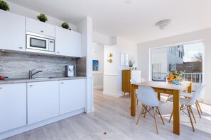 Een moderne keuken met witte kasten, een ingebouwde magnetron en een houten eettafel met stoelen.