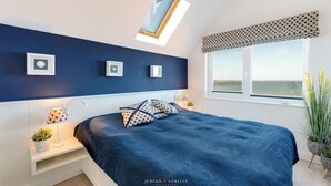 Une chambre à coucher avec une tête de lit bleu foncé, un puits de lumière, une grande fenêtre donnant sur un beau paysage et des lampes de chevet.