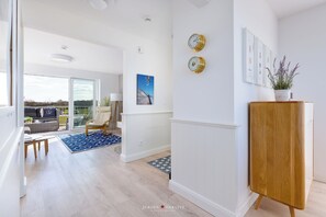 Een moderne woonkamer met een groot raam, een houten kast en een blauw tapijt met patroon.