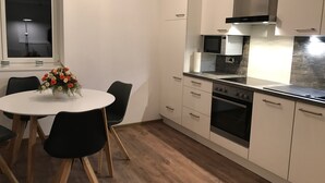 A modern kitchen with white cabinets, a black countertop, and a wooden dining table with chairs. - Beautiful barrier-free 3 1/2 room apartment near the beach!  (Allensbach)