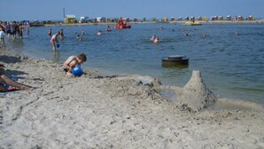 A beach with people swimming and playing in the water, a sandcastle, and beachgoers in the background.