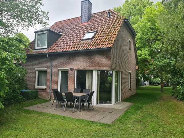 Ein zweigeschossiges Backsteinhäuschen mit einem Ziegeldach, einer Terrasse mit Tisch und Stühlen und einem grünen Rasen.