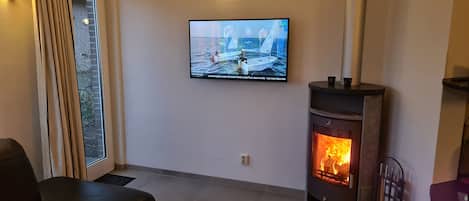 Una sala de estar acogedora con chimenea, televisor montado en la pared y una ventana con cortinas.