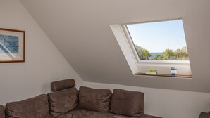 A room with a sloped ceiling and a skylight, a brown sofa, and a framed picture on the wall. - 3-Bedroom Apartment  (Grömitz)