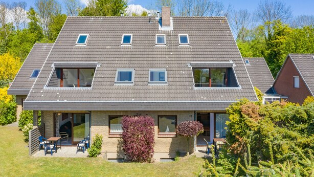 A modern two-story house with a sloped roof, large windows, and a small patio area with outdoor seating. - 3-Bedroom Apartment  (Grömitz)