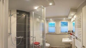 A modern bathroom with a glass-enclosed shower, a toilet, a sink, and a window with a view.