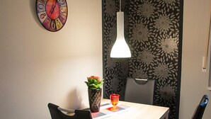 A dining area with a wooden table, black chairs, a colorful clock, a pendant light, and a potted plant.