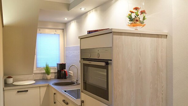 A compact kitchen with a built-in oven, a sink, and a window with blinds.
