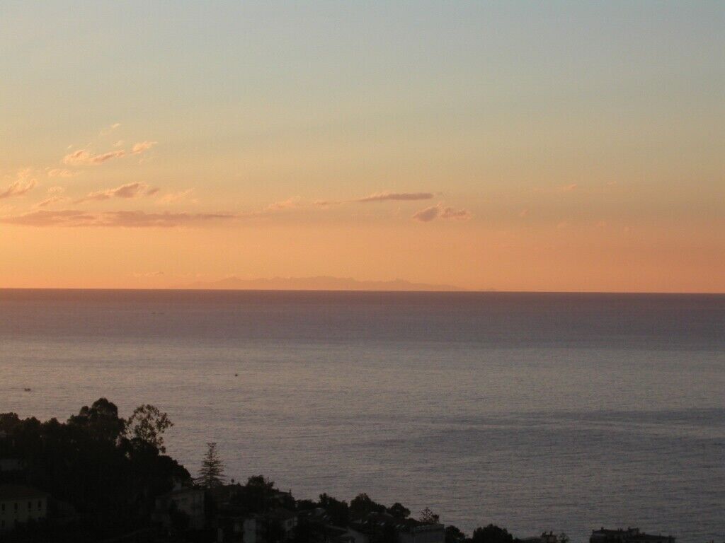 A coastal view during sunset with a calm sea and distant mountains.