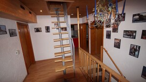 Un escalier en bois avec une rampe métallique, un lustre et plusieurs photographies encadrées accrochées aux murs.