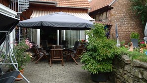 Une terrasse extérieure avec une table et des chaises, un espace salon abrité et des plantes en pot.