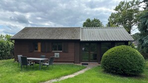 Une cabane en bois avec un toit en tuiles, un petit porche et un coin repas avec des chaises.