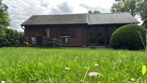 Une cabane en bois avec un toit en pente, une petite véranda avec une table et des chaises, et une pelouse bien entretenue.