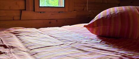 A wooden cabin room with a bed, a window, and a ceiling light fixture.