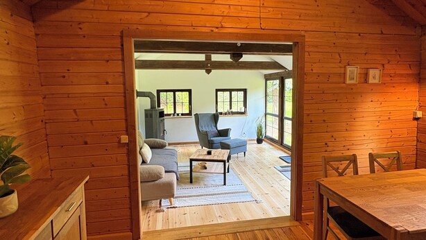 L’intérieur d’un chalet en bois comprend un coin repas, une cuisine et une vue sur l’extérieur, visible à travers une porte ouverte.