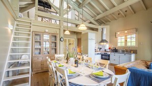 A spacious dining area with a high ceiling and exposed beams, a kitchen with modern appliances, and a cozy seating area with a blue tablecloth.