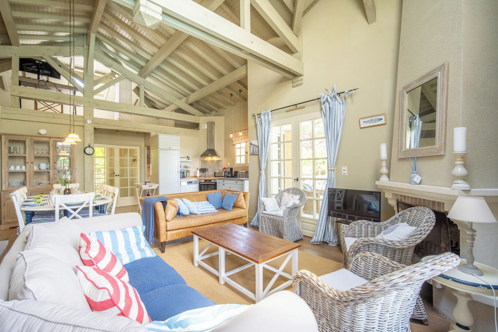 A spacious living area with a high ceiling, a fireplace, wicker furniture, and a dining area with a table and chairs.