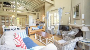 A spacious living area with a high ceiling, a fireplace, wicker furniture, and a dining area with a table and chairs.
