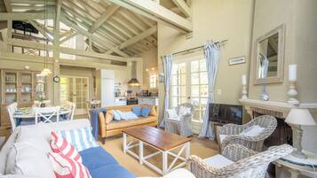 A spacious living area with a high ceiling, a fireplace, wicker furniture, and a dining area with a table and chairs.