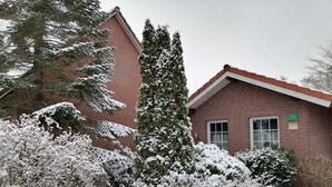 A brick building with a red roof, surrounded by snow-covered trees and bushes.