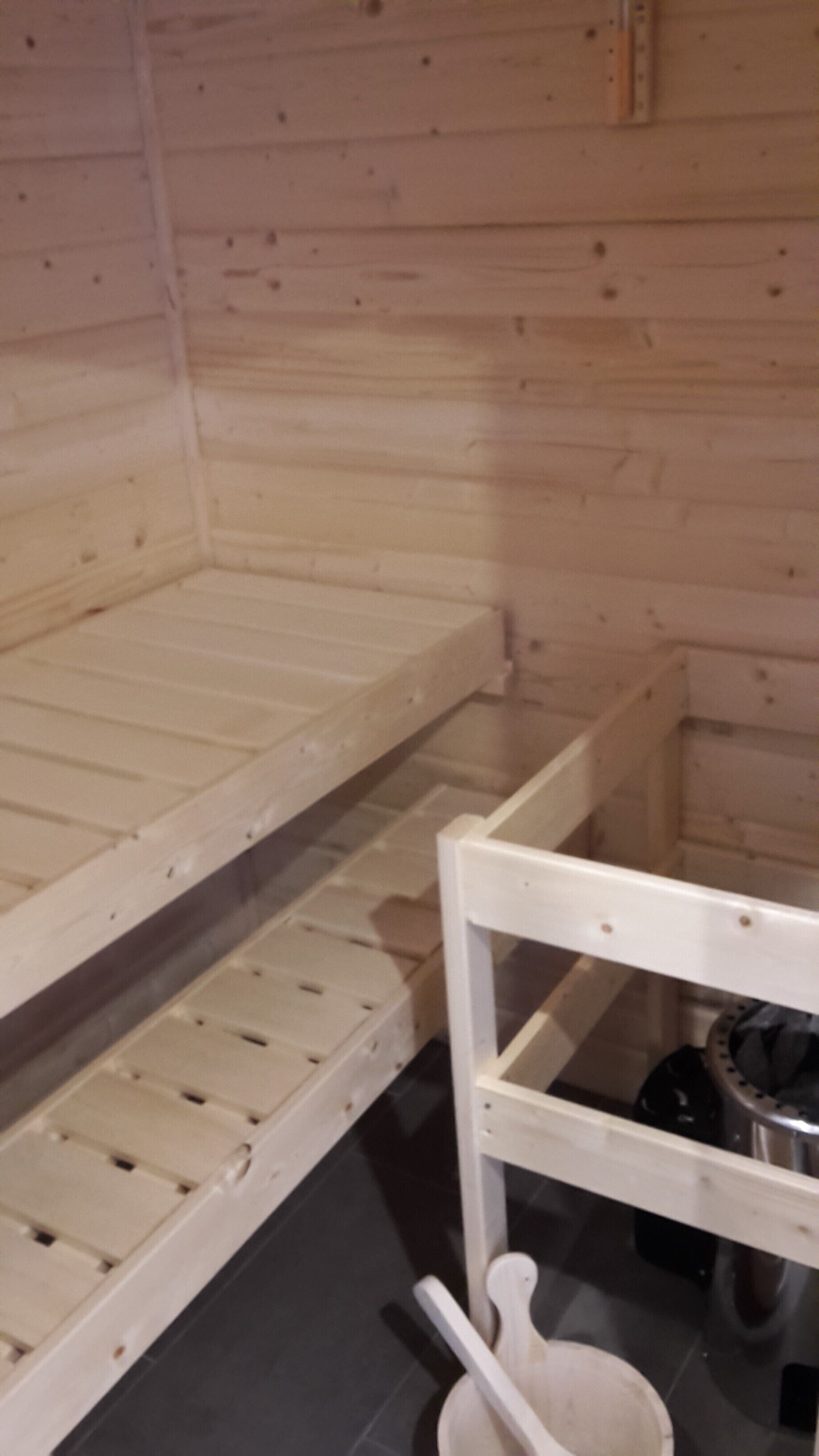 Puinen mökki, jonka sisätiloissa on kerrossänky ja pieni pöytä, jonka päällä on metallinen kattila.