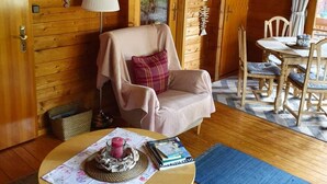 A cozy cabin interior with a wooden interior, a dining area with a table and chairs, and a small round table with a lamp and books.