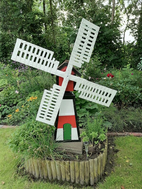 A windmill sculpture in a garden with surrounding greenery and flowers.