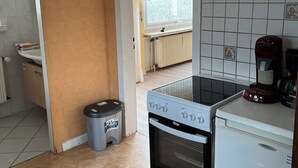 Une cuisine équipée d’une cuisinière, d’un four et d’un réfrigérateur. On y trouve également une poubelle et une fenêtre avec des rideaux.