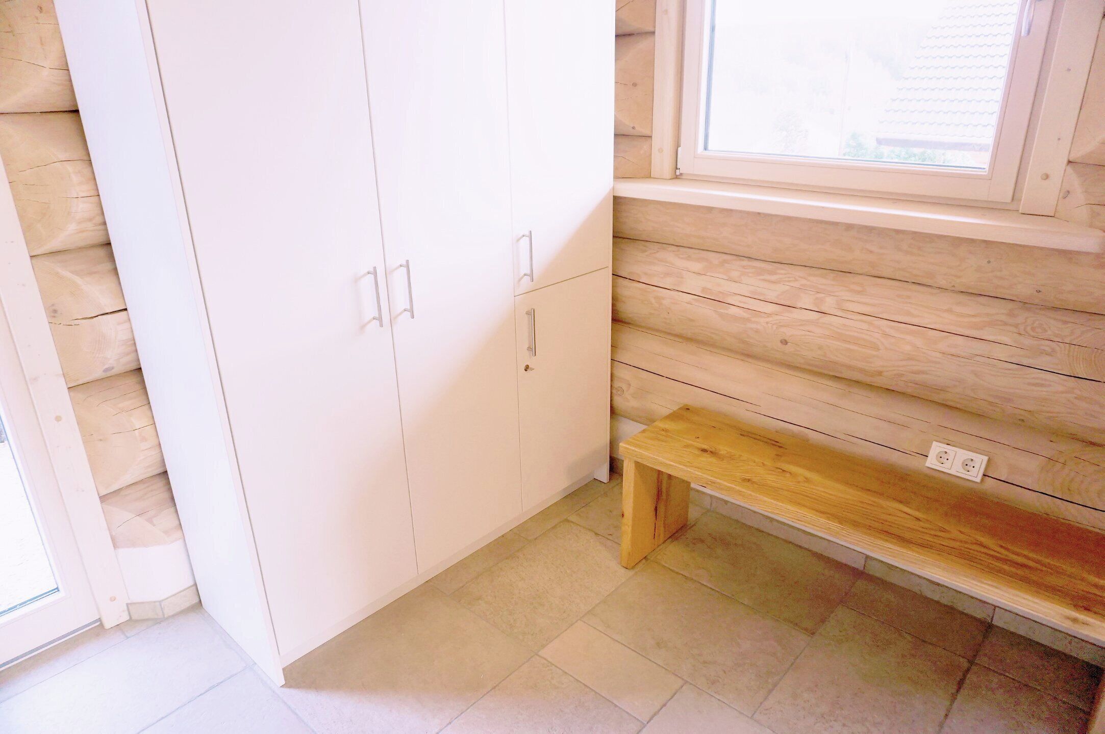Ein Zimmer mit einer hölzernen Bank, einem weißen Kleiderschrank und einem Fenster mit Jalousien.