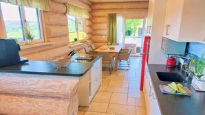 A log cabin interior with a kitchen, dining area, and a view of the outdoors. - Canadian log cabins in the Hunsrück with lake and national park views (Langweiler)