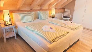 A bedroom with a wooden ceiling, two beds with striped bedding, bedside lamps, a chair, and a wardrobe. - Canadian log cabins in the Hunsrück with lake and national park views (Langweiler)