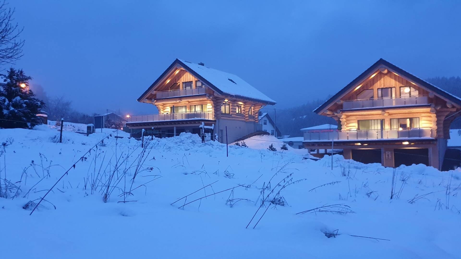 Duas casas no estilo de cabana de toras, com varandas, rodeadas de neve.