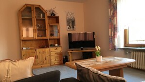 Een woonkamer met een houten kast, een televisie, een salontafel met een plant en twee banken.