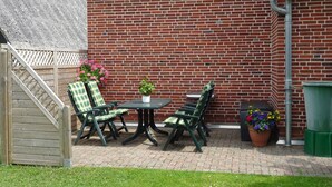 Een terras met een bakstenen muur, een tafel met stoelen en potplanten.