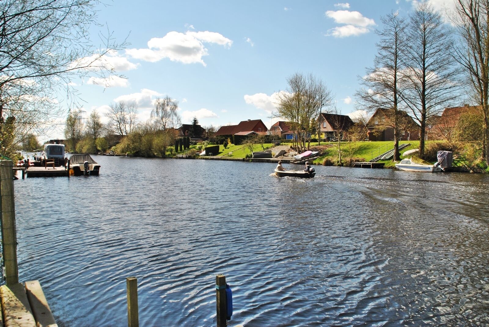 Ein ruhiger Fluss mit Booten, einem Steg und Häusern im Hintergrund.