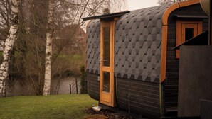 Un piccolo chalet moderno con tetto curvo e porta in legno, immerso tra alberi e un'area erbosa.