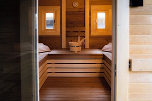 Uma sala de sauna com bancos de madeira, um balde de madeira e um relógio na parede.
