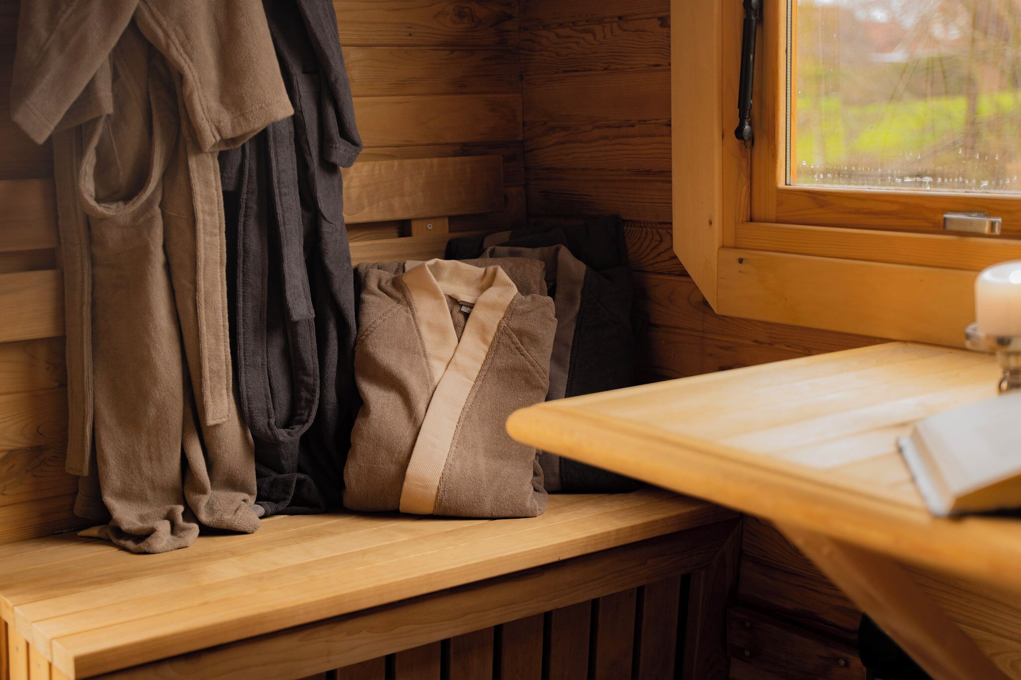 A wooden bench with a cushion and a robe hanging on the wall.