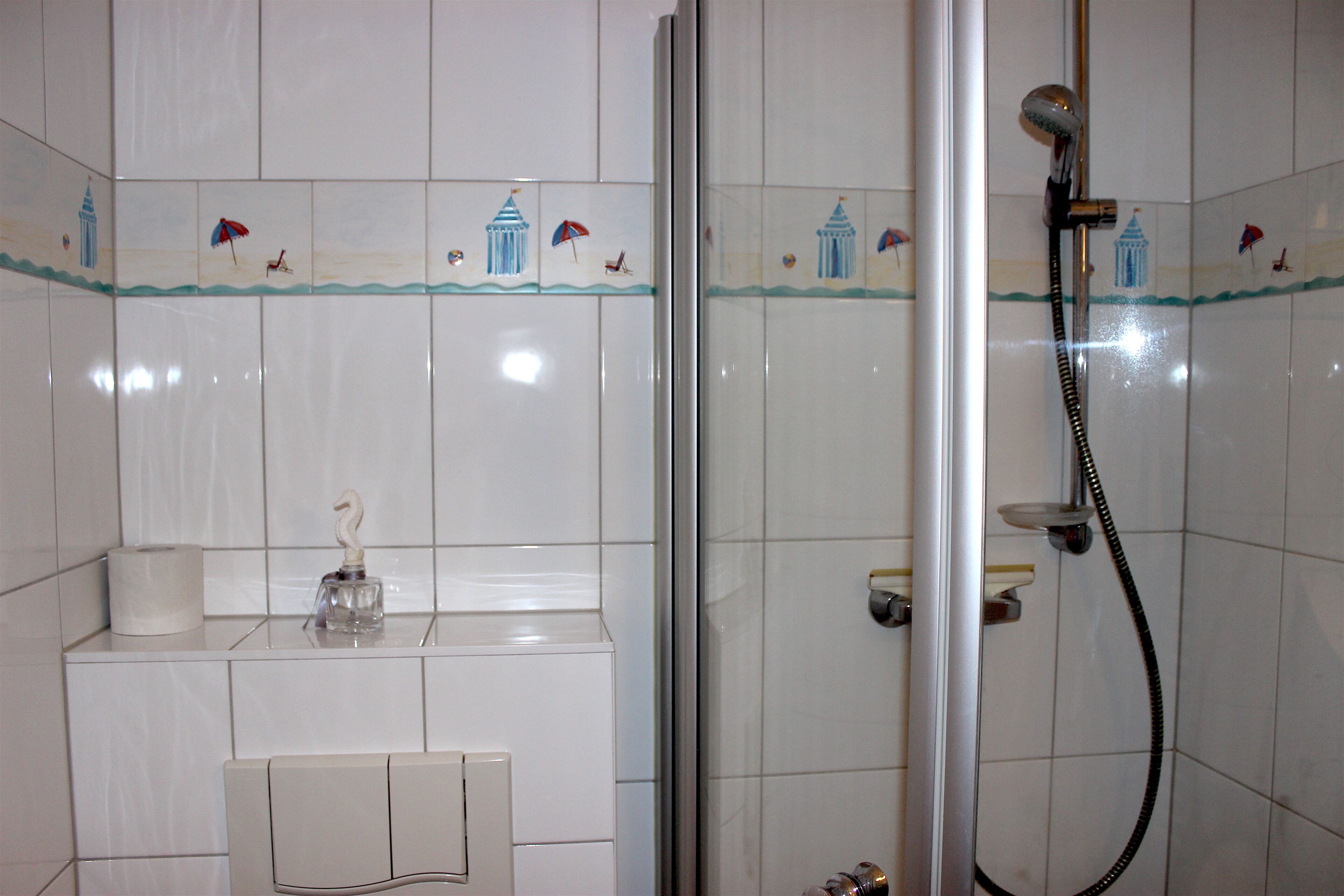 A bathroom with white tiles, a shower, a toilet, and a sink with a soap dispenser.