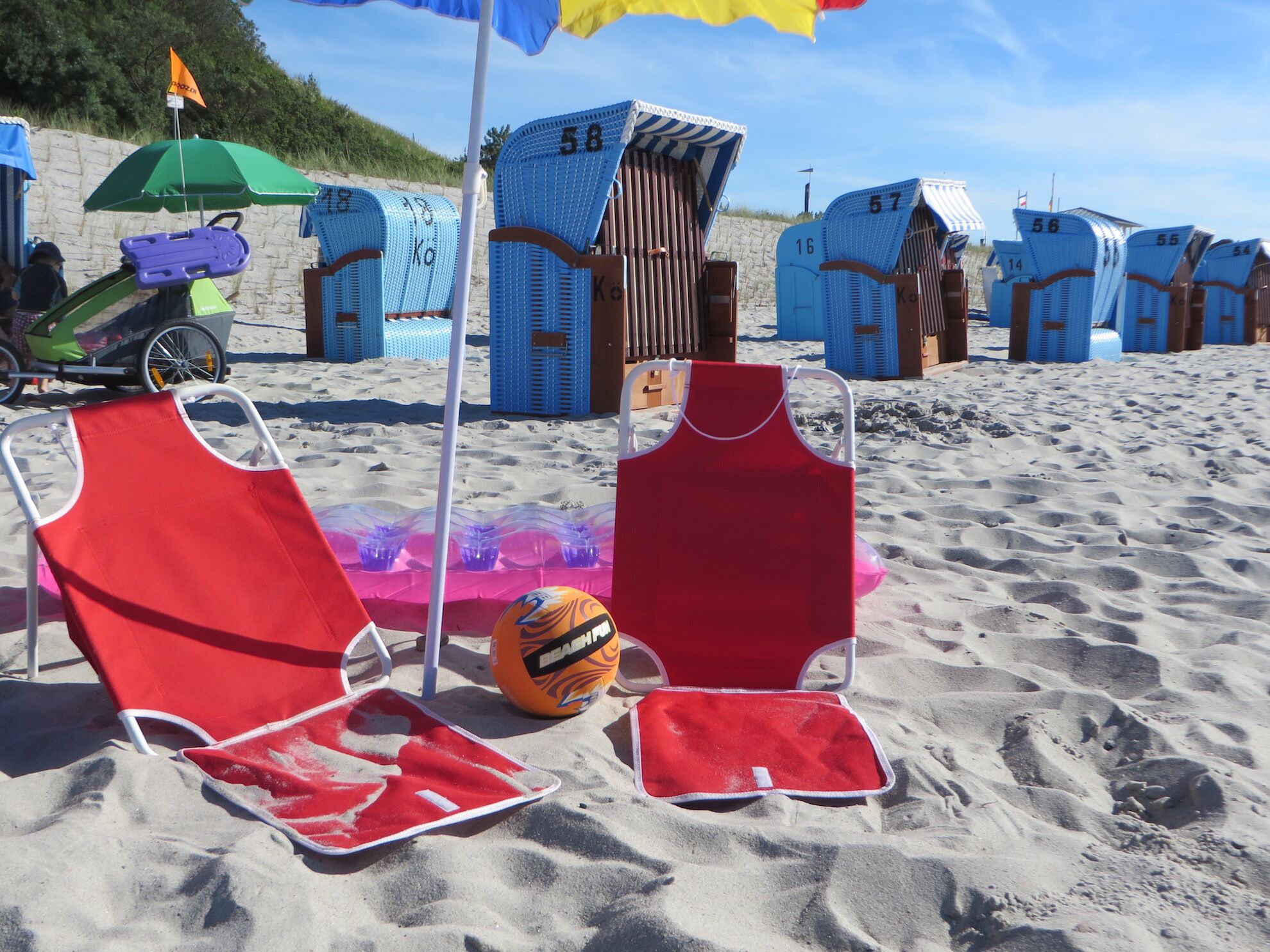 Strandstühle, ein Volleyballnetz und Strandkörbe am Sandstrand.