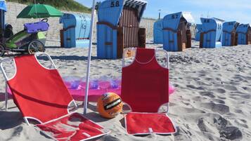 Strandstühle, ein Volleyballnetz und Strandkörbe am Sandstrand.
