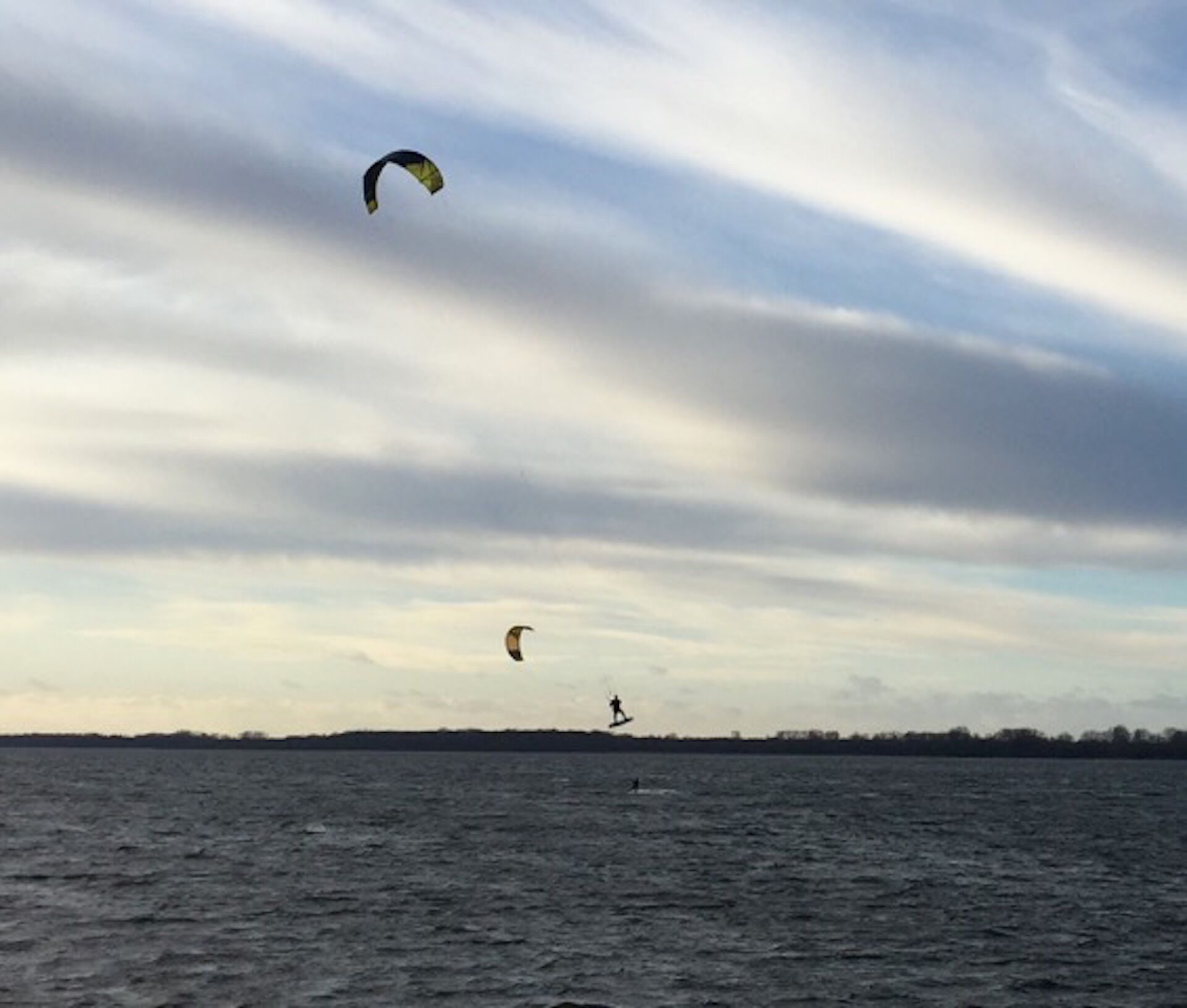 Ein Gewässer mit einem Kitesurfer und einem Schwimmer.