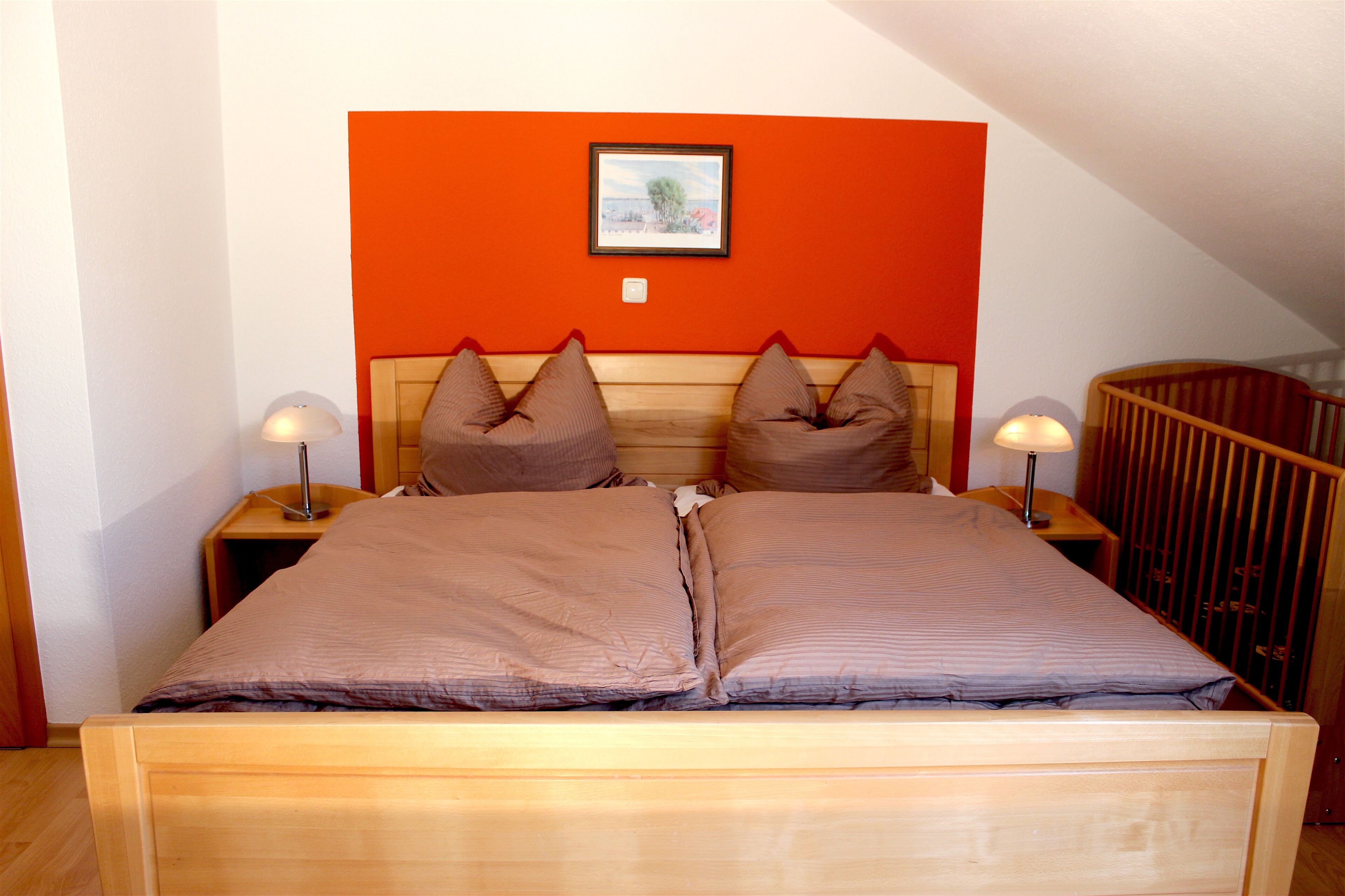 Ein Doppelbett mit Holzrahmen, zwei Nachttische mit Lampen und ein gerahmtes Bild an der Wand.