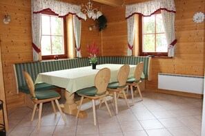 En matsal i en stuga med träpanel, ett bord dukat för fyra personer, gröna sittdynor på stolarna och en bänk.