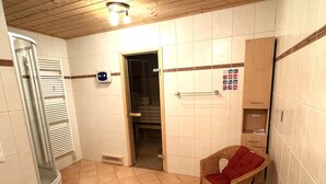 A bathroom with a shower, a towel rack, a wicker chair with a red cushion, and a tiled floor. - Exclusive vacation home in the Nockberge with a sauna and fireplace (Patergassen)