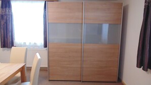 Una habitación con un armario de madera, una silla blanca y una mesa de madera.