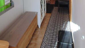 Un pasillo estrecho con un banco, un tapete estampado, un armario con puerta decorativa y una cama al fondo.